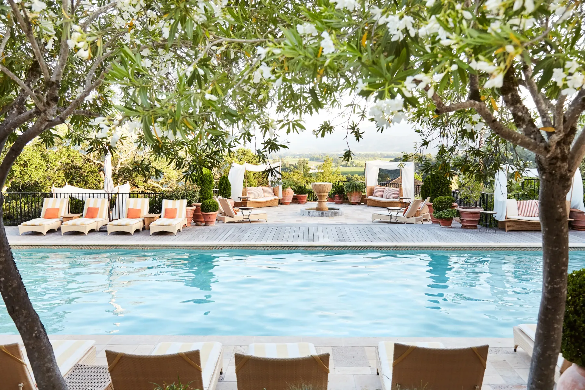 Pool framed by oleanders, striped loungers with orange cushions, cabanas, fountain, and valley hills, at Auberge du Soleil in Napa Valley.