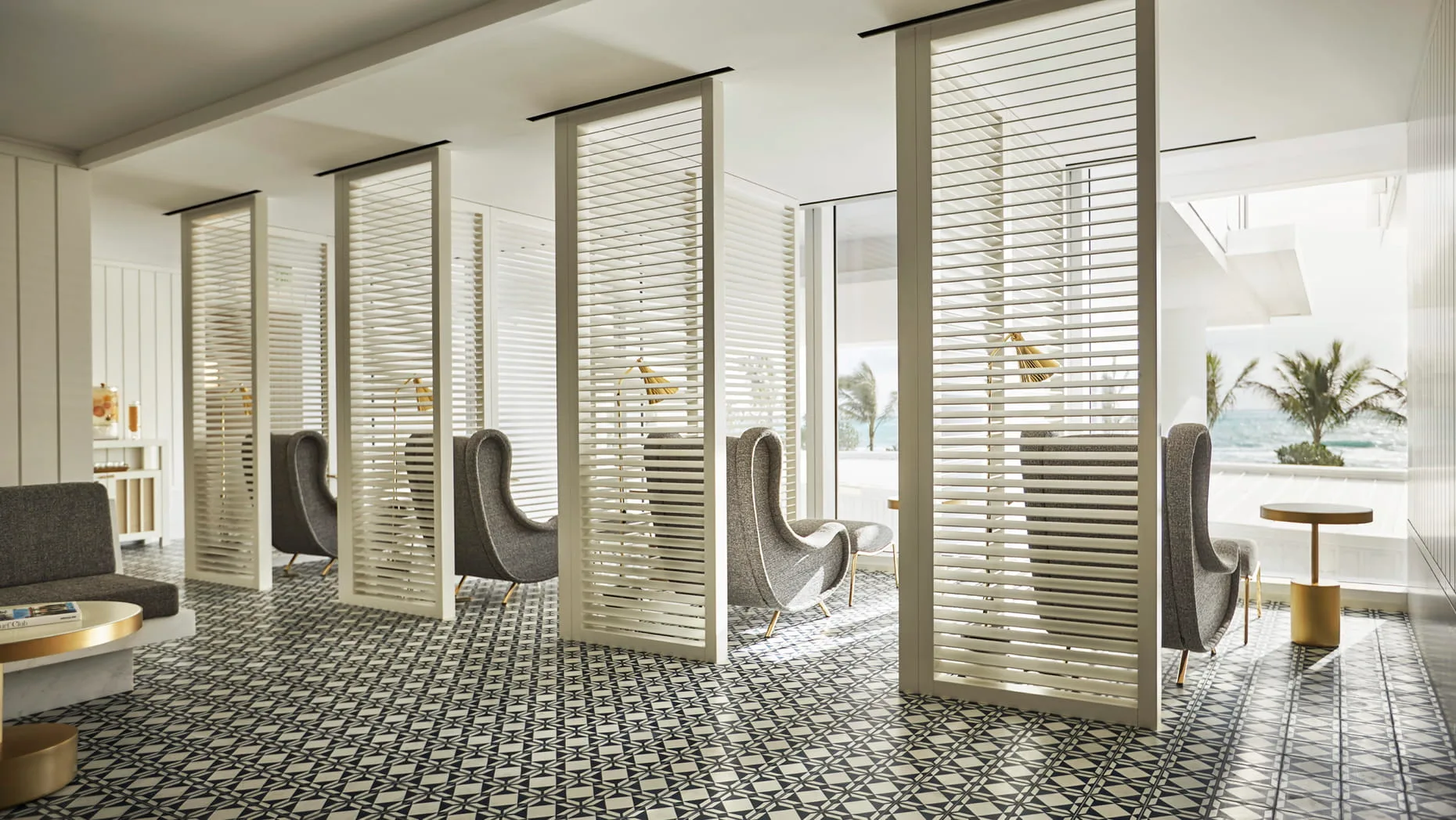 Bright relaxation lounge with slatted screens, wingback chairs, tile floor, and ocean-view windows at Four Seasons Hotel at The Surf Club