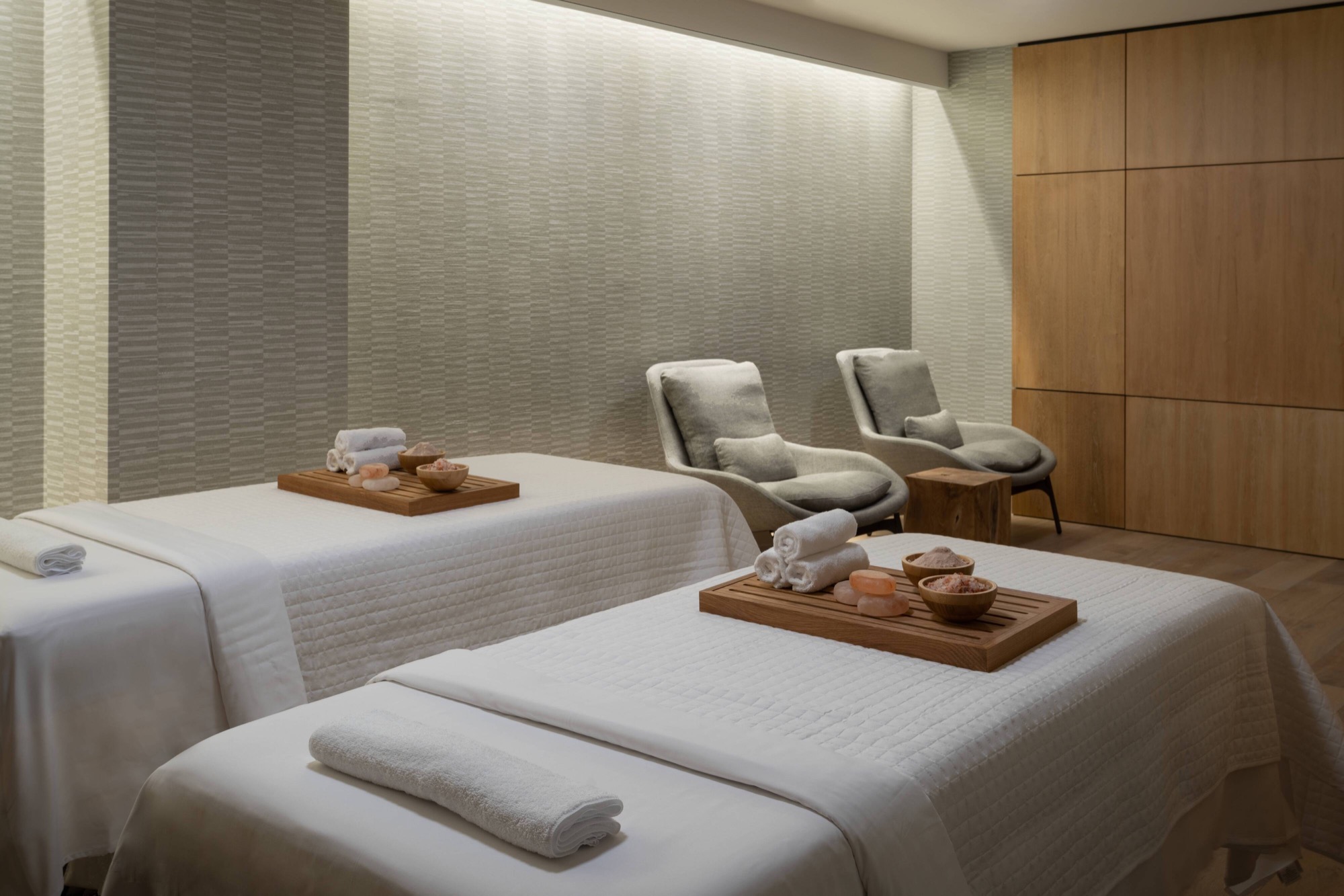 Two treatment tables with white quilted covers and rolled towels sit in a pale room.