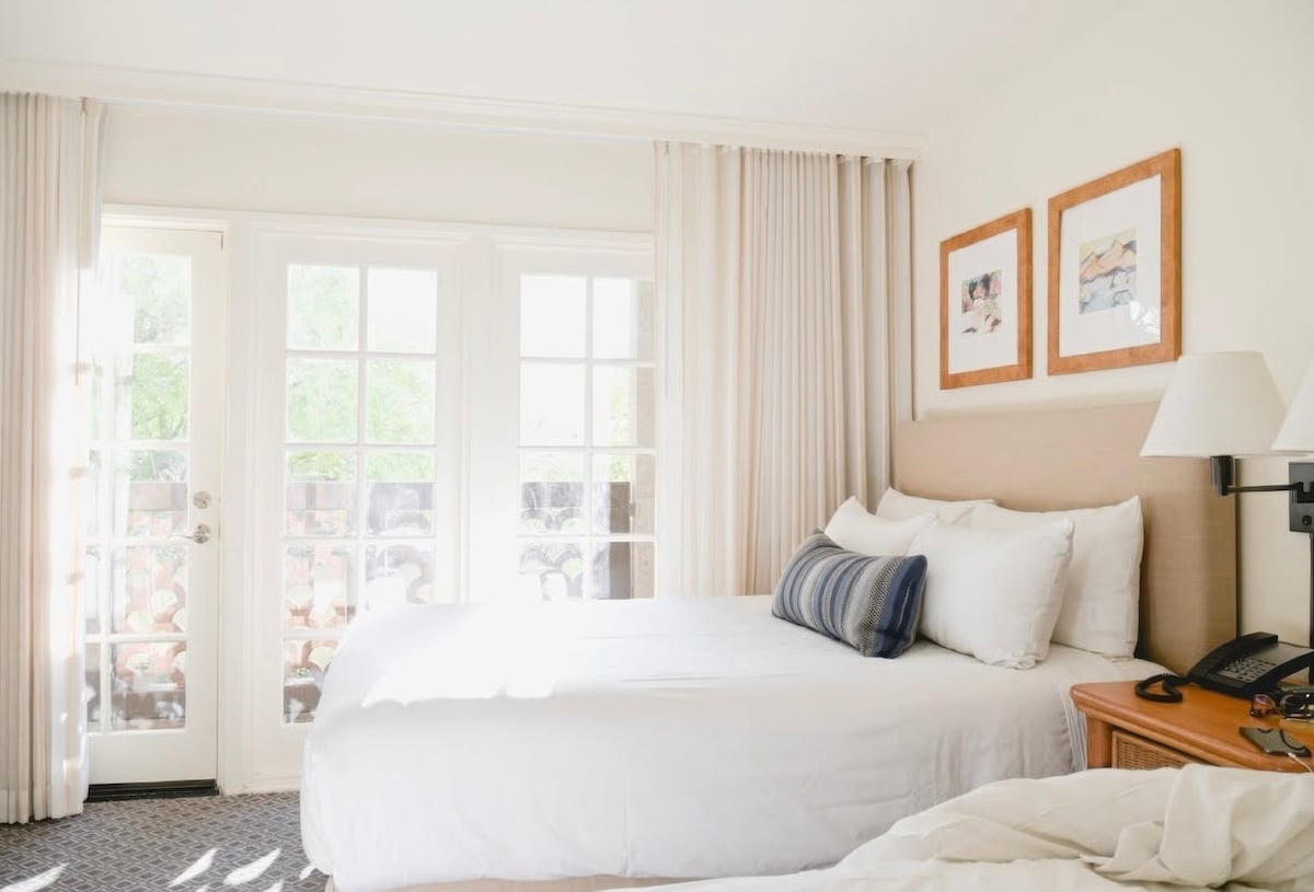 Bright white guest room with linen headboard, blue accent pillow and French doors to balcony at Arizona Grand Resort & Spa, Phoenix