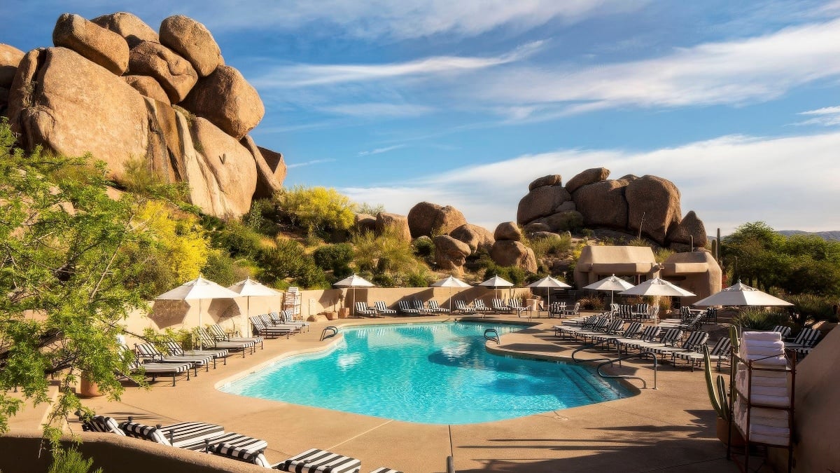 Main resort pool with black-and-white striped loungers and white parasols framed by granite boulders at Boulders Resort & Spa Scottsdale, Scottsdale
