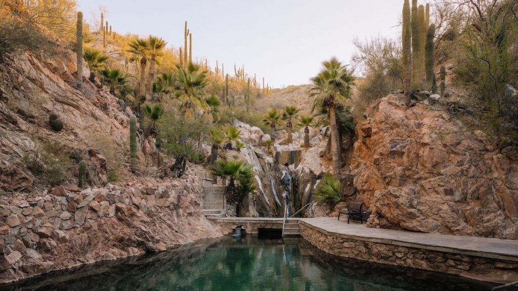Upper hot spring pool carved into rock with waterfall, saguaros, and fan palms at Castle Hot Springs, Morristown