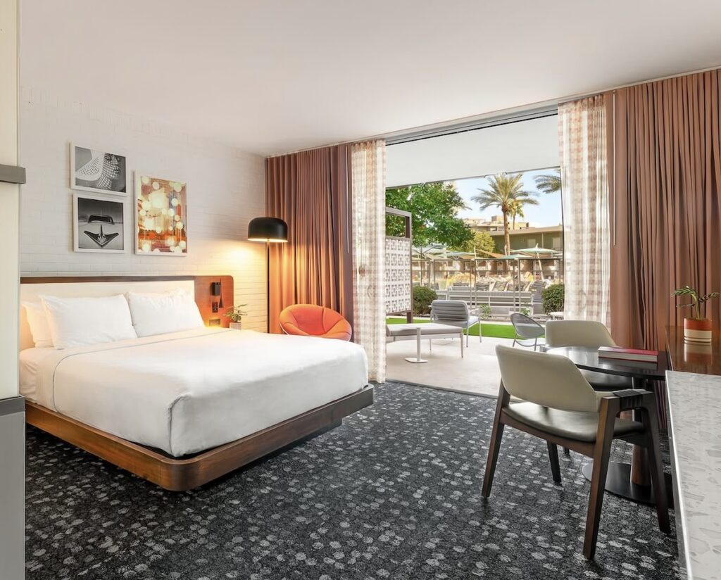 King guest room with walnut platform bed, orange womb chair, retro artwork, and poolside patio at Hotel Valley Ho, Scottsdale