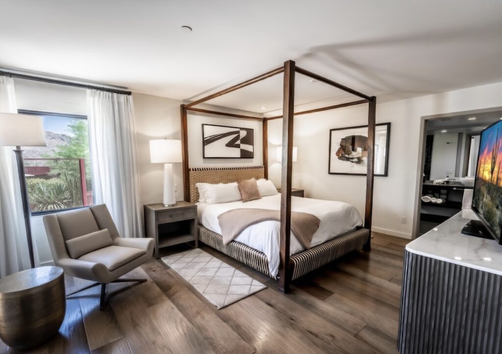 Guest room with walnut four-poster bed, woven rattan headboard, and hardwood floors at Sanctuary Camelback Mountain Resort & Spa, Scottsdale