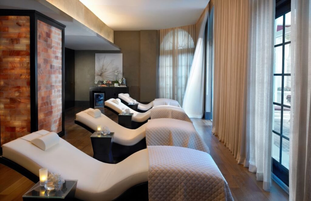Spa relaxation lounge with white curved loungers and backlit Himalayan salt wall at Acqualina Resort & Residences, Sunny Isles Beach