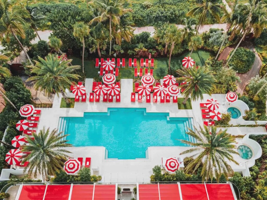 Aerial view of pool deck with red-and-white striped umbrellas and palm gardens at Faena Hotel Miami Beach