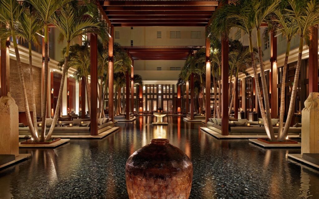 Grand lobby at night with reflective water feature, tall palms and dark teak columns at The Setai, Miami Beach