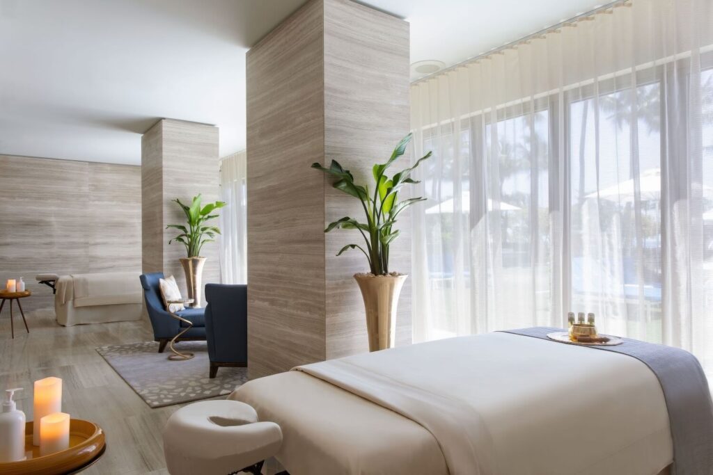 Light-filled spa treatment room with linen-draped massage table, tropical plants and sheer garden views, The St. Regis Bal Harbour Resort