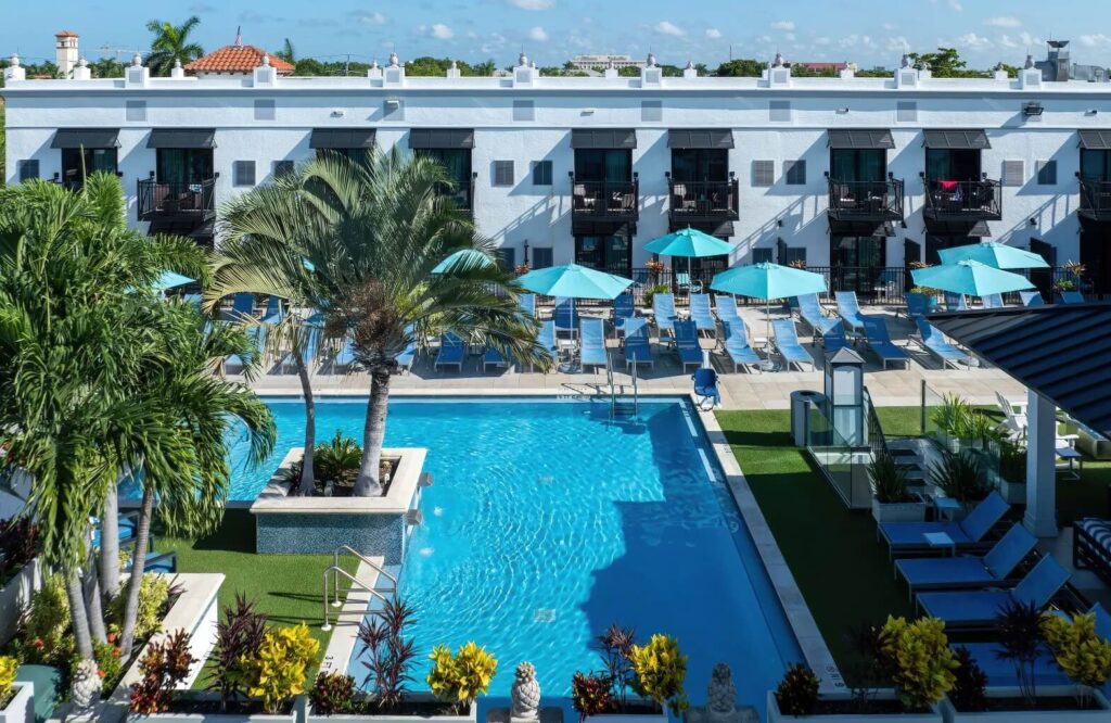 Aerial view of outdoor pool with blue loungers and umbrellas beside white hotel building at Inn on Fifth, Naples Florida