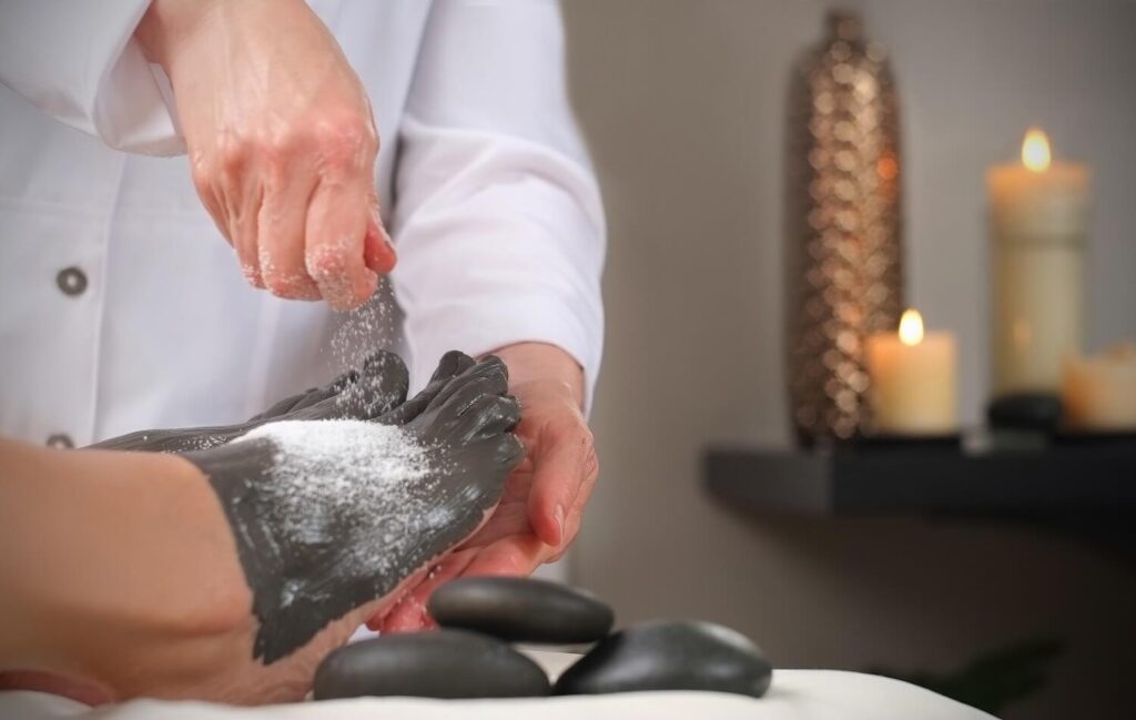 Spa therapist applying dark mud body wrap with salt scrub over hot stones at Inn on Fifth, Naples Florida