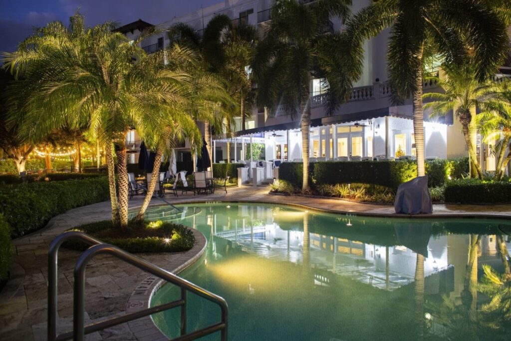Night-time pool courtyard illuminated by palm uplighting and lantern-lit dining area at Inn at Pelican Bay, Naples, Florida.