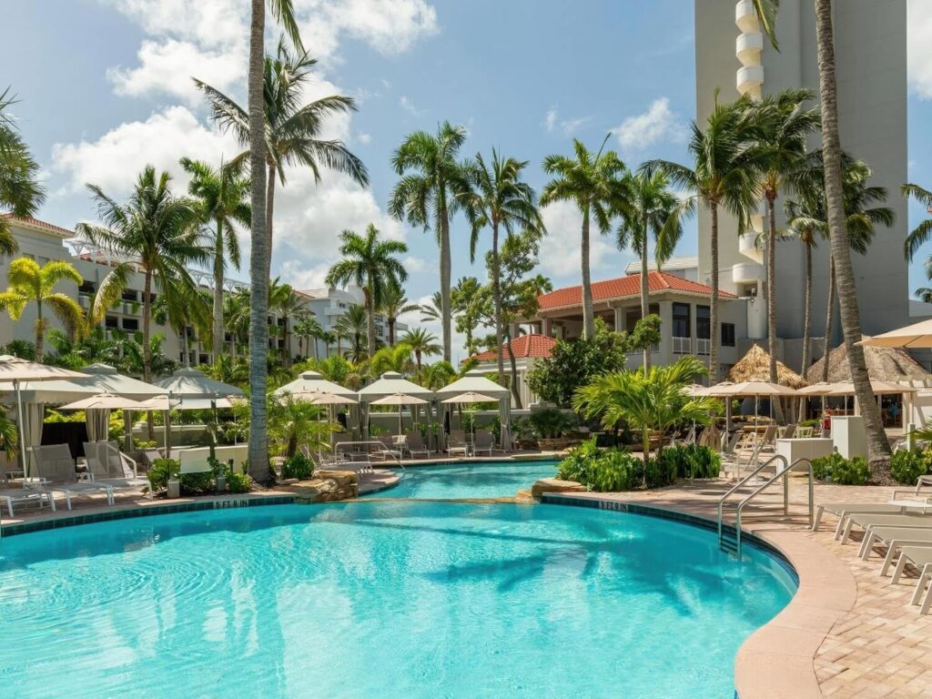Main freeform pool with cream umbrellas and sun loungers amid tall palm grove at LaPlaya Beach & Golf Resort, Naples Florida