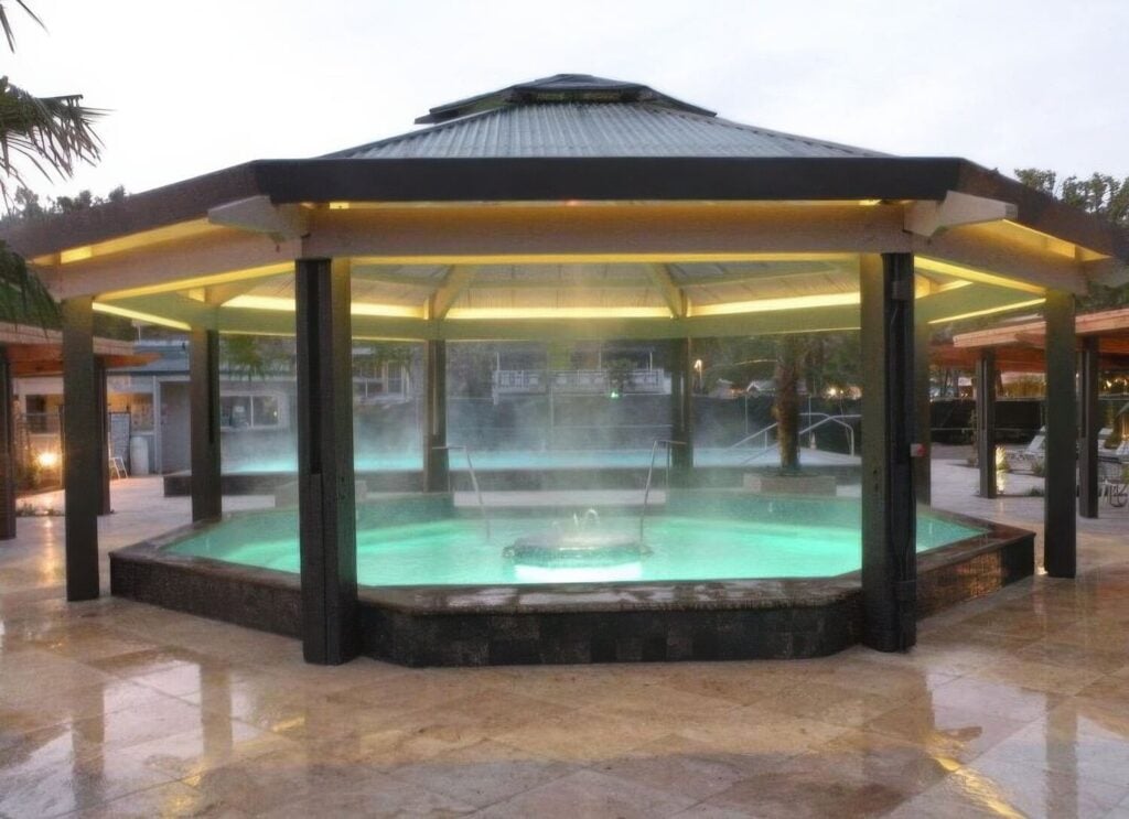 Steaming octagonal covered geothermal soaking pool glowing green at dusk at Calistoga Spa Hot Springs, Calistoga