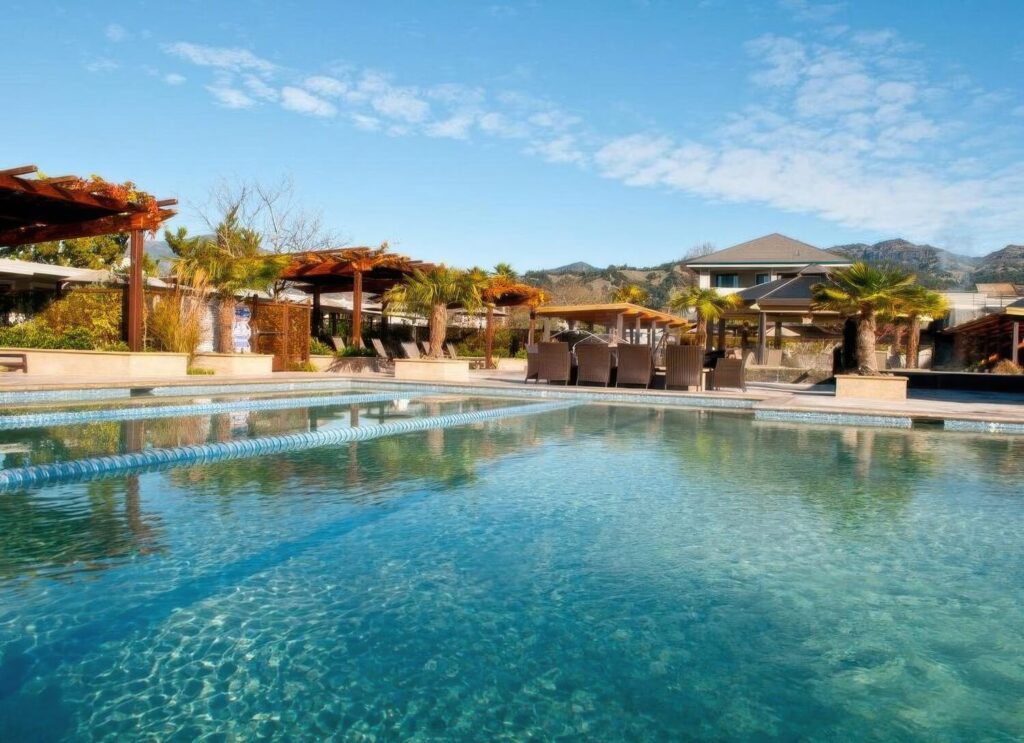 Mineral pool ringed by wood pergolas, palms and dining tables below the mountains at Calistoga Spa Hot Springs, Calistoga