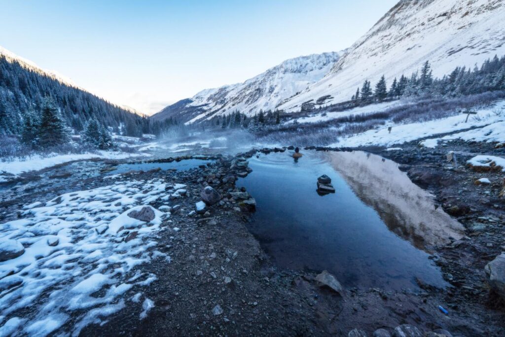 A lone bather in a rock-rimmed hot pool amid snow-capped peaks at Conundrum Hot Springs, Colorado