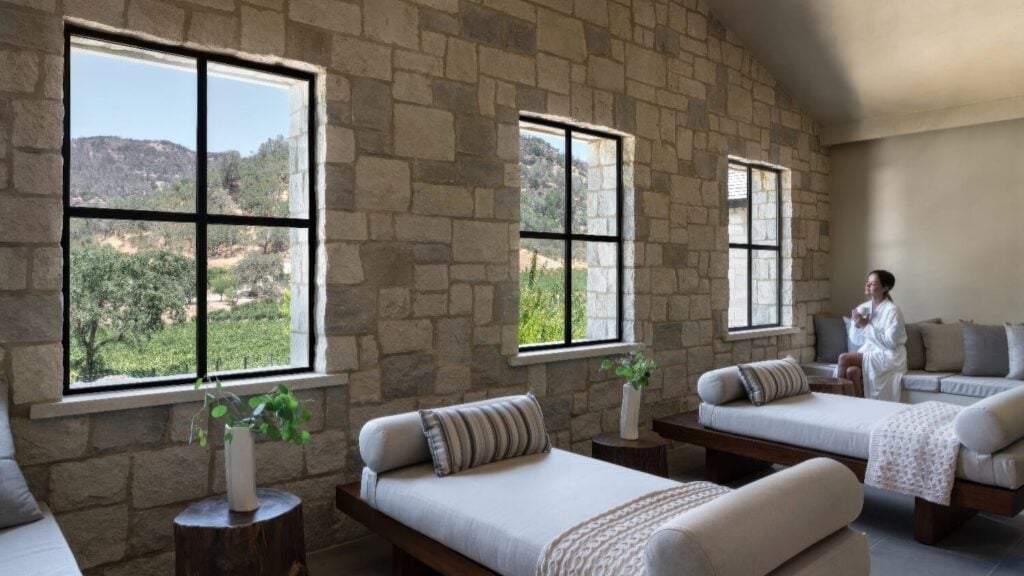 Stone-walled spa relaxation lounge with linen daybeds and vineyard views at Four Seasons Resort Napa Valley, Calistoga