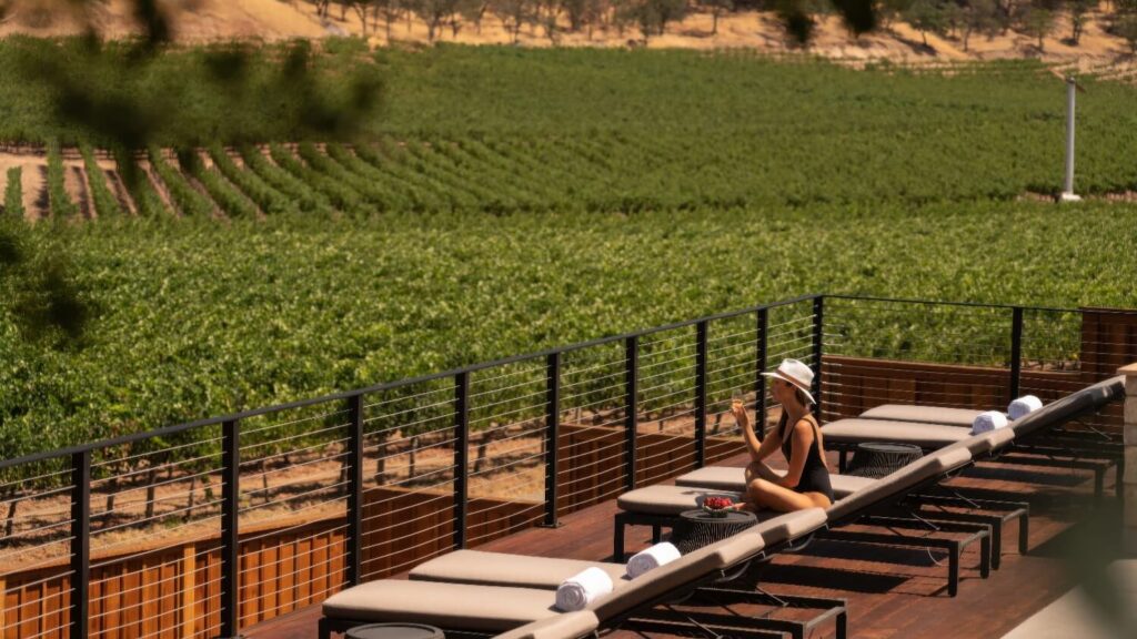 Guest relaxing on a sun-deck lounger with wine above the vineyards at Four Seasons Resort Napa Valley, Calistoga