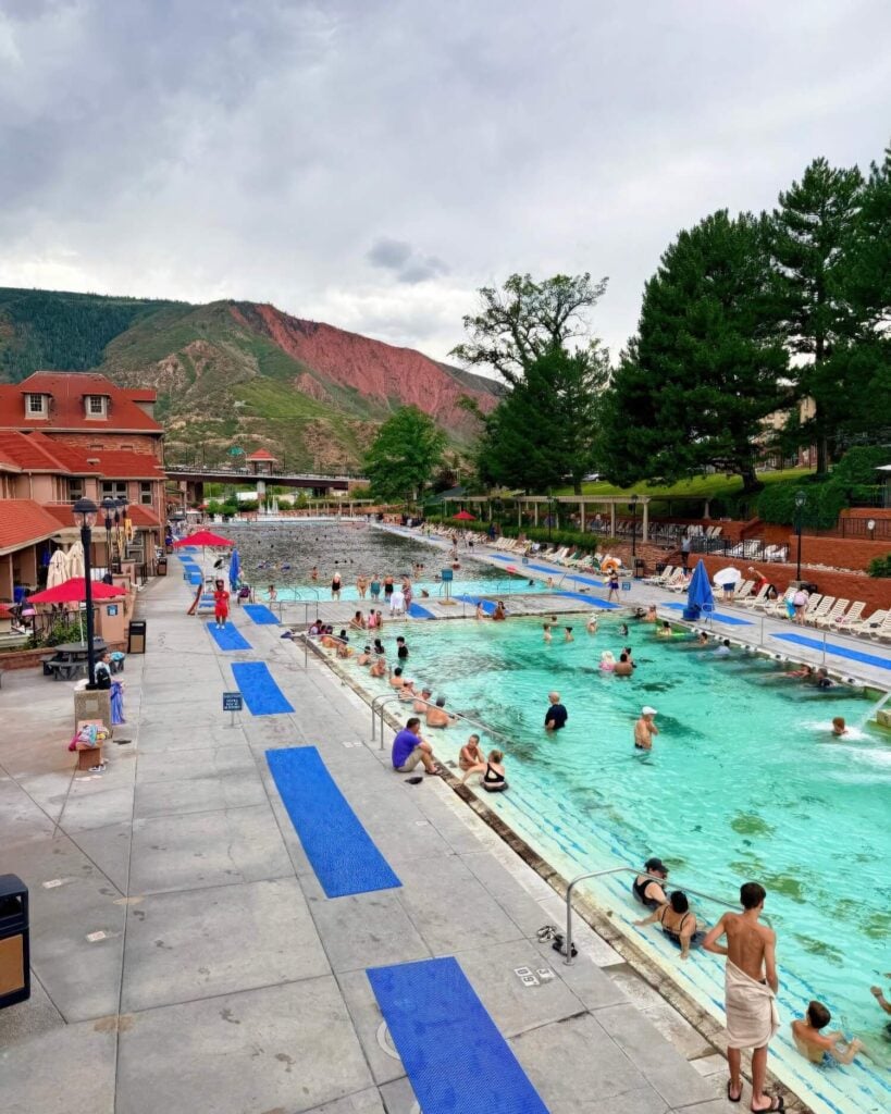 Bathers in the vast hot springs pool below the red-faced mountain at Glenwood Hot Springs, Colorado