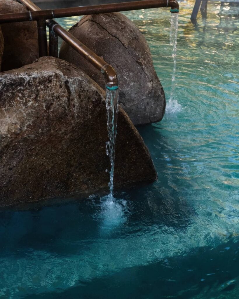 Mineral water pouring through copper spouts over boulders into a turquoise soaking pool at Ojo Caliente, New Mexico