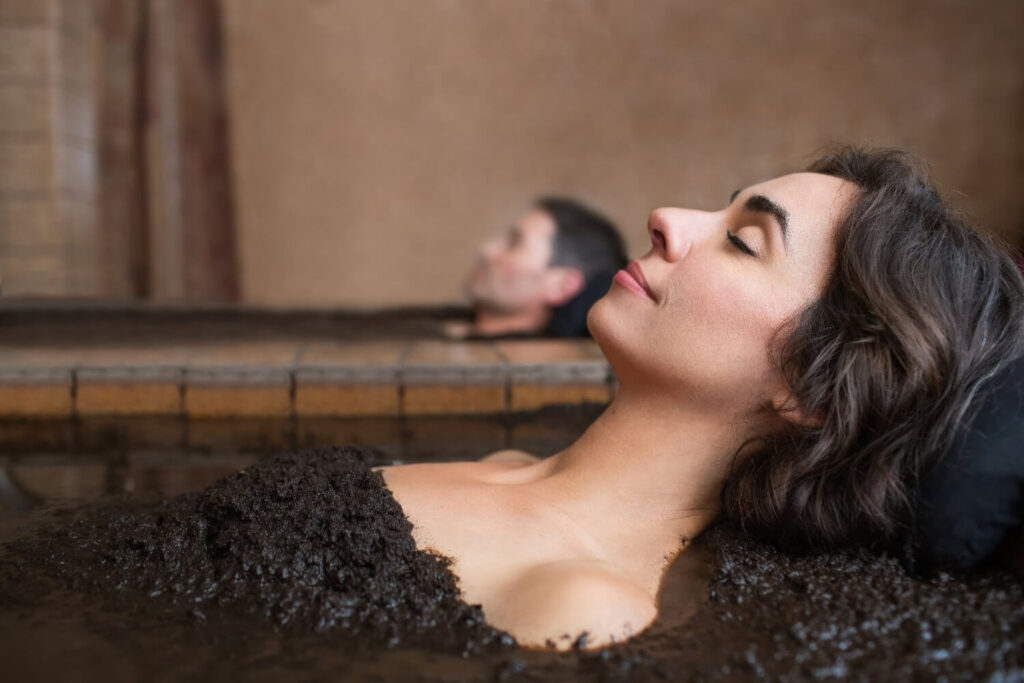 Couple relaxing side by side in a volcanic-ash mud bath at Roman Spa Hot Springs Resort, Calistoga