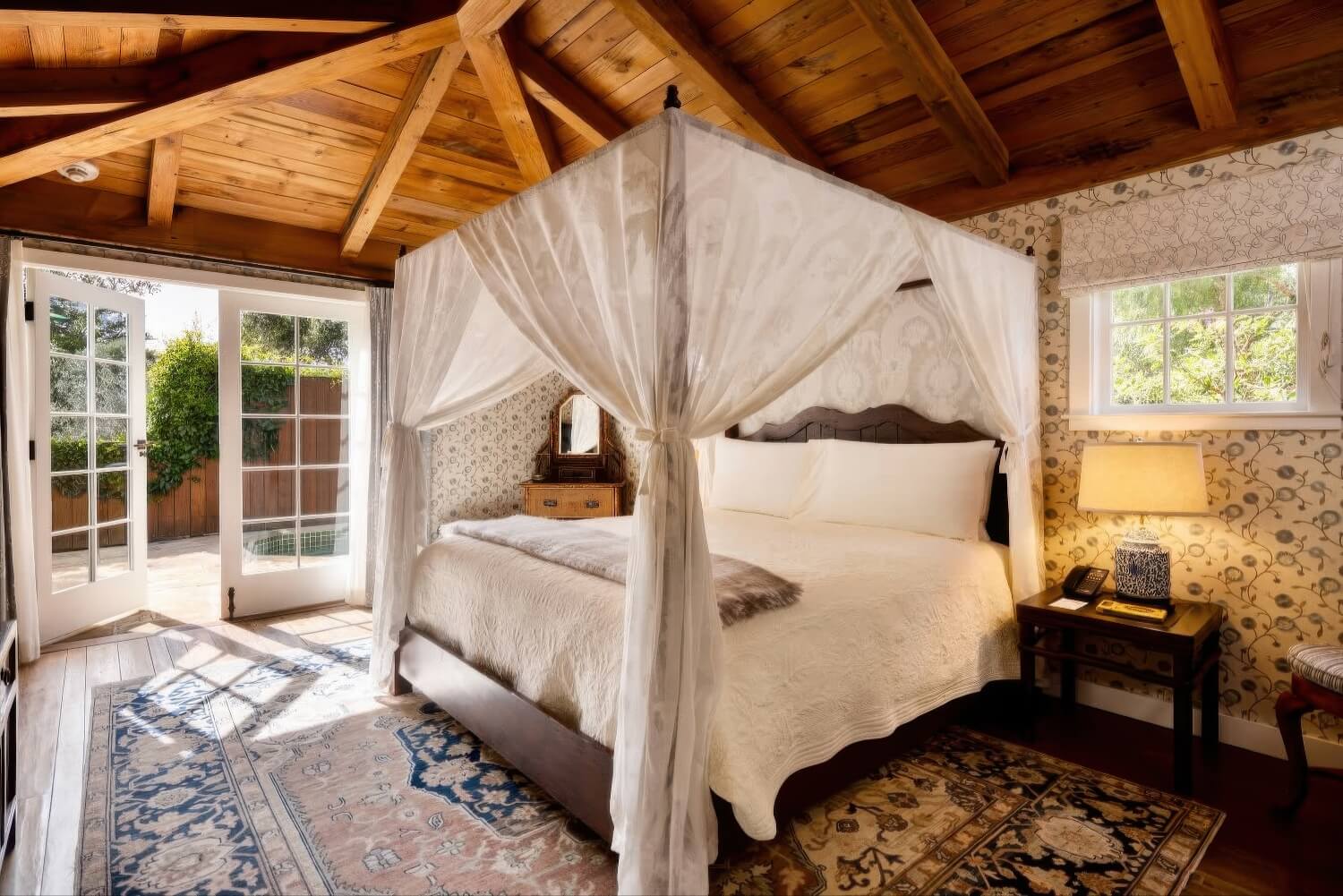 Cottage bedroom with a white canopy bed and French doors opening to a private plunge-pool patio at San Ysidro Ranch, Montecito