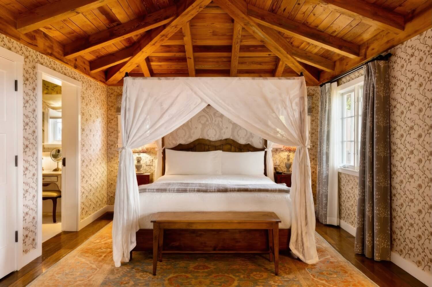 Cottage bedroom with a white-draped canopy bed, timber ceiling and floral wallpaper at San Ysidro Ranch, Montecito