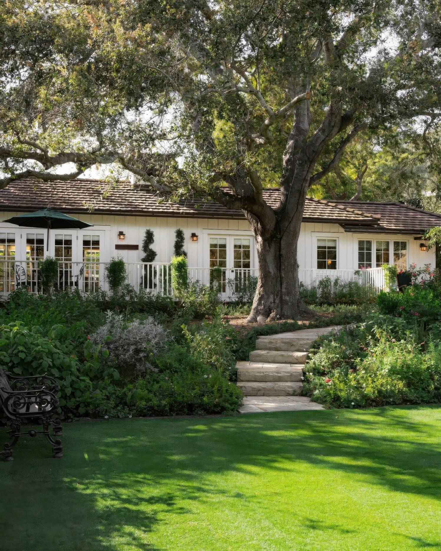 White board-and-batten cottage beneath a sprawling heritage oak and cottage gardens at San Ysidro Ranch, Montecito