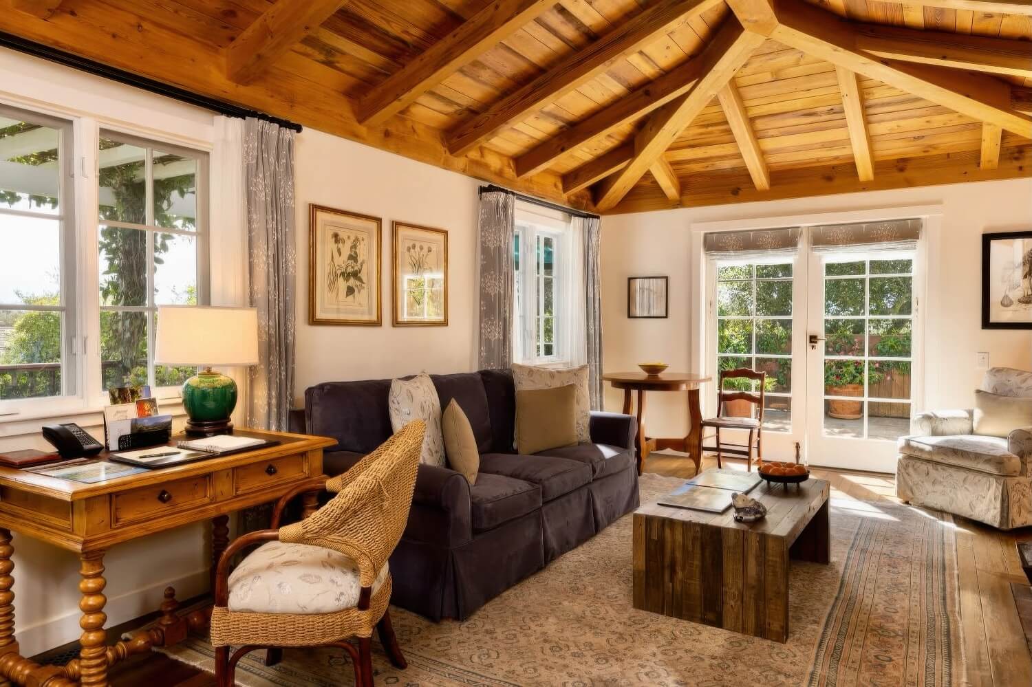 Cottage living room with an exposed timber-beam ceiling, dark sofa and French doors to the garden at San Ysidro Ranch, Montecito