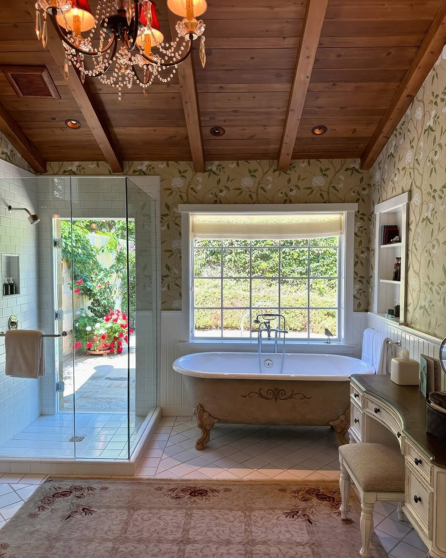 Guest bathroom with a roll-top tub, glass shower, floral wallpaper and a crystal chandelier at San Ysidro Ranch, Montecito