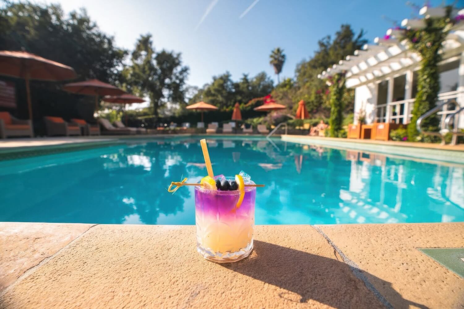 Colourful cocktail on the pool coping beside orange umbrellas and loungers at San Ysidro Ranch, Montecito