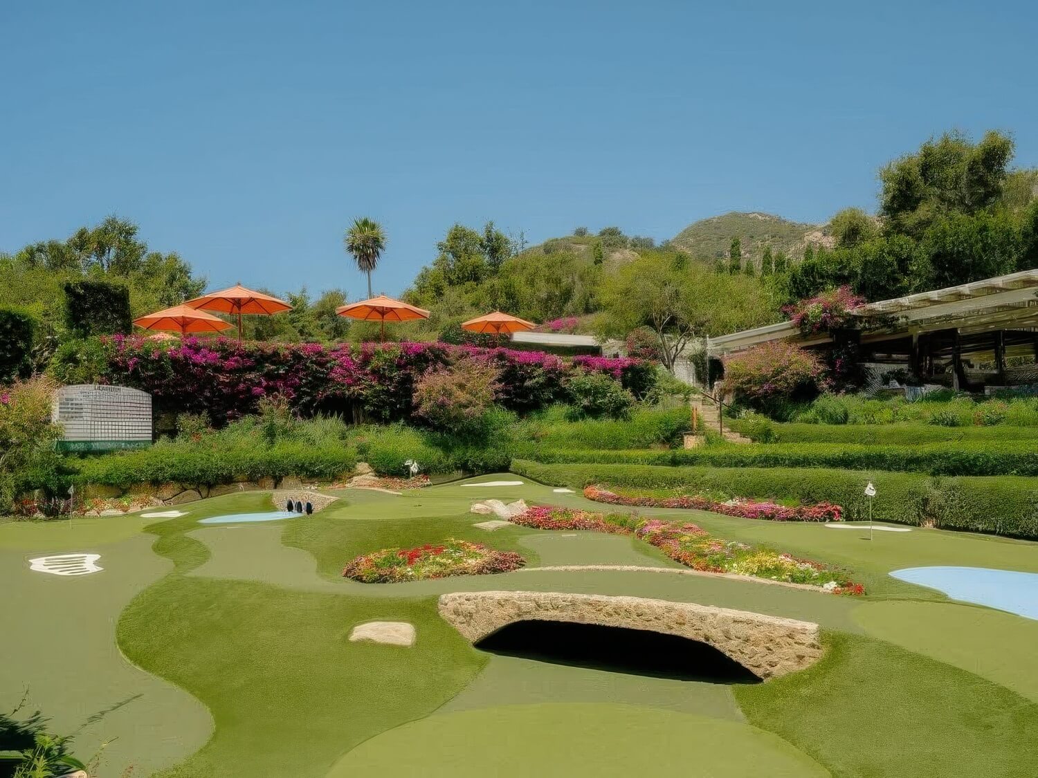 Landscaped putting green with orange umbrellas, a stone bridge and bougainvillea at San Ysidro Ranch, Montecito