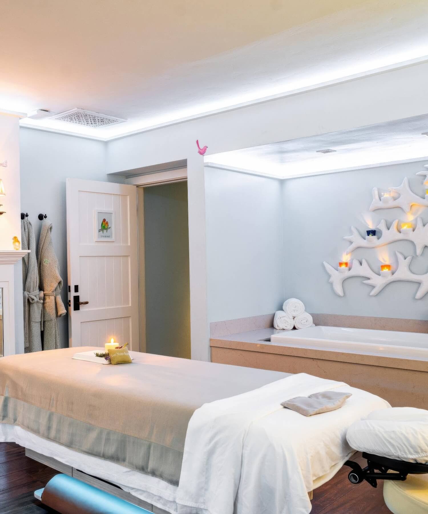 Spa treatment room with a massage table, soaking tub and antler candle sconce at San Ysidro Ranch, Montecito