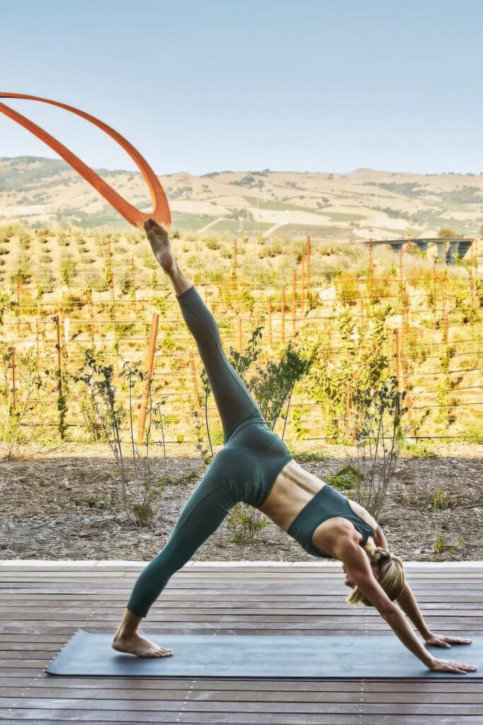 Guest practising yoga on a deck above the vineyards and Corten sculpture at Stanly Ranch, Auberge Resorts Collection, Napa