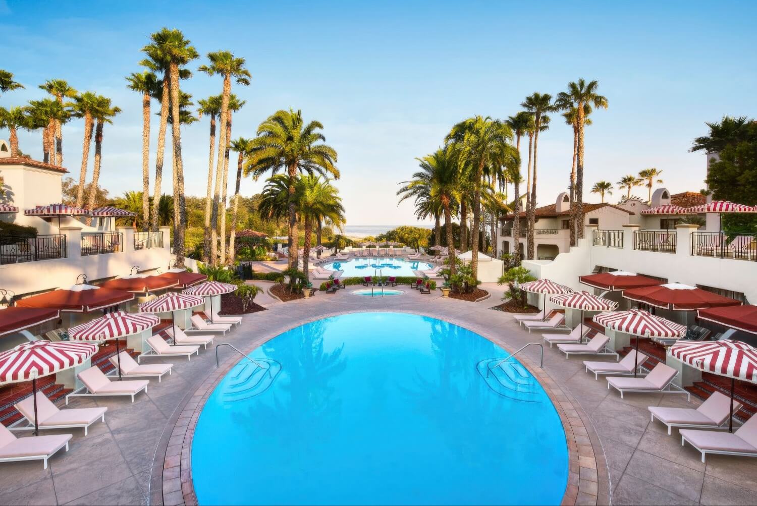 Round resort pool ringed by red-and-white striped cabanas and palms at sunset, The Ritz-Carlton Bacara, Santa Barbara