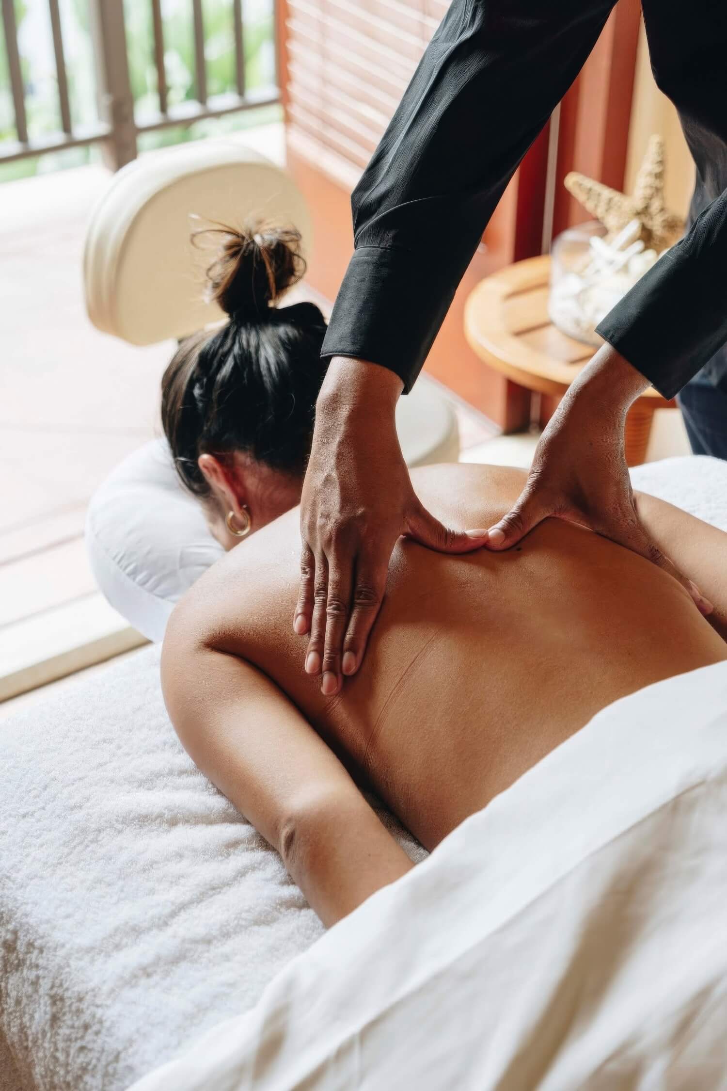 Therapist giving a guest a back massage on a spa table by a shuttered window at The Ritz-Carlton Bacara, Santa Barbara