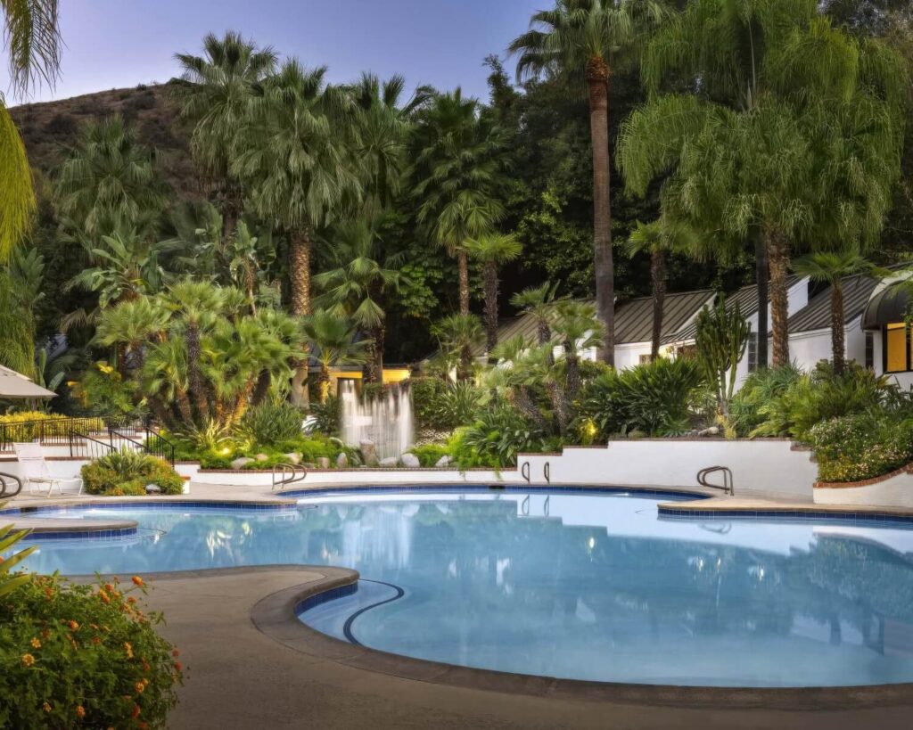Palm-ringed mineral pool with a rock waterfall glowing at dusk at Glen Ivy Hot Springs, Corona, California