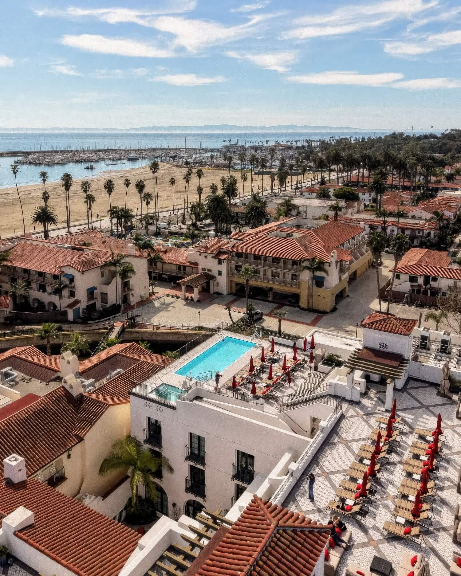 Overhead view of the rooftop pool and sun deck above red-tile roofs, the beach and harbor at Hotel Californian, Santa Barbara