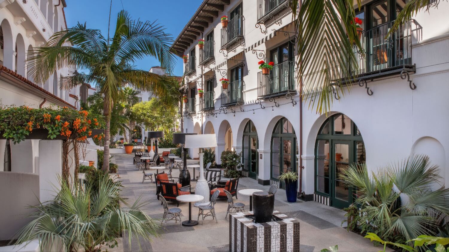 Arched courtyard terrace with geranium-filled balconies and bistro seating at Hotel Californian, Santa Barbara