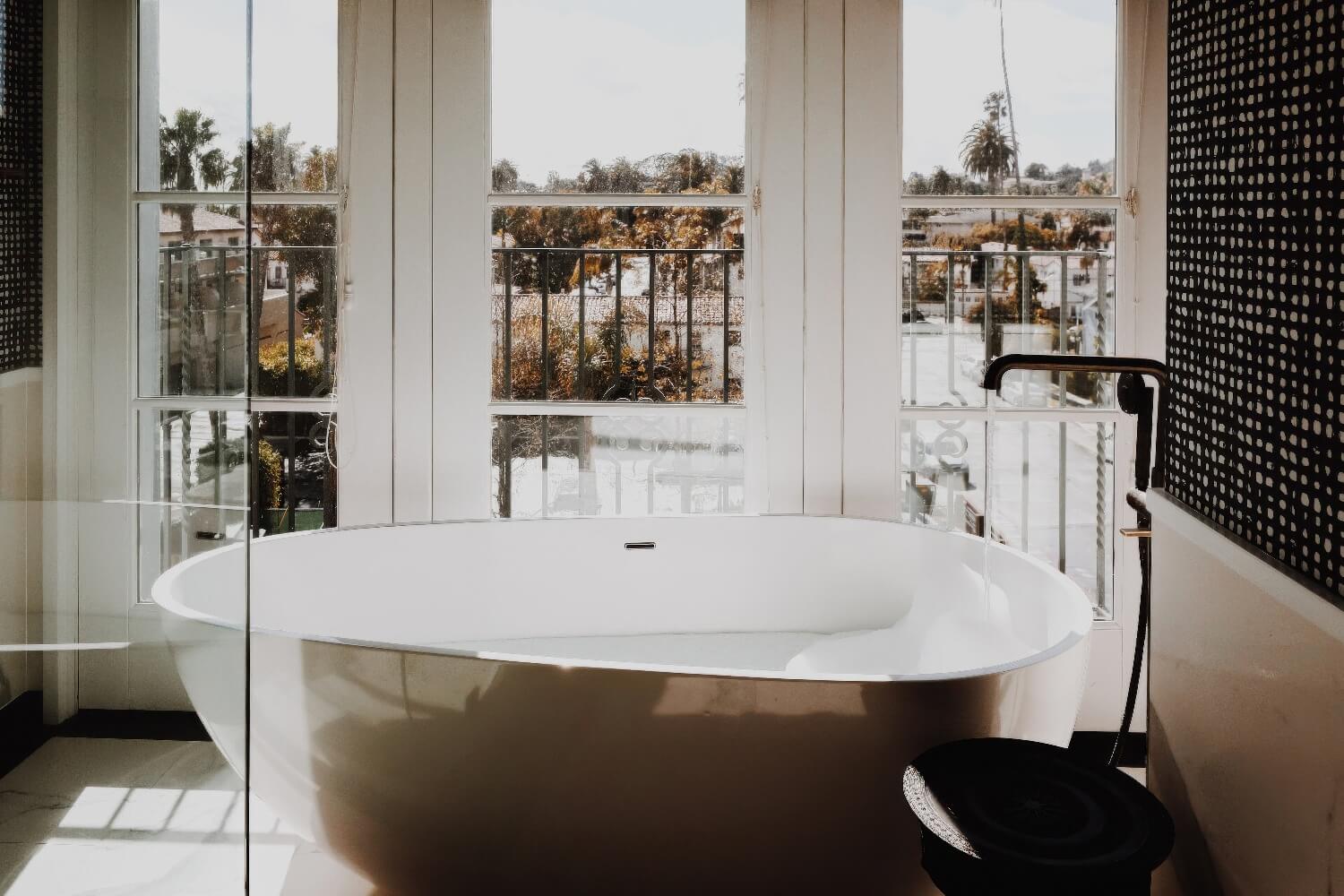 Freestanding oval tub set before balcony windows overlooking red-tile rooftops at Hotel Californian, Santa Barbara