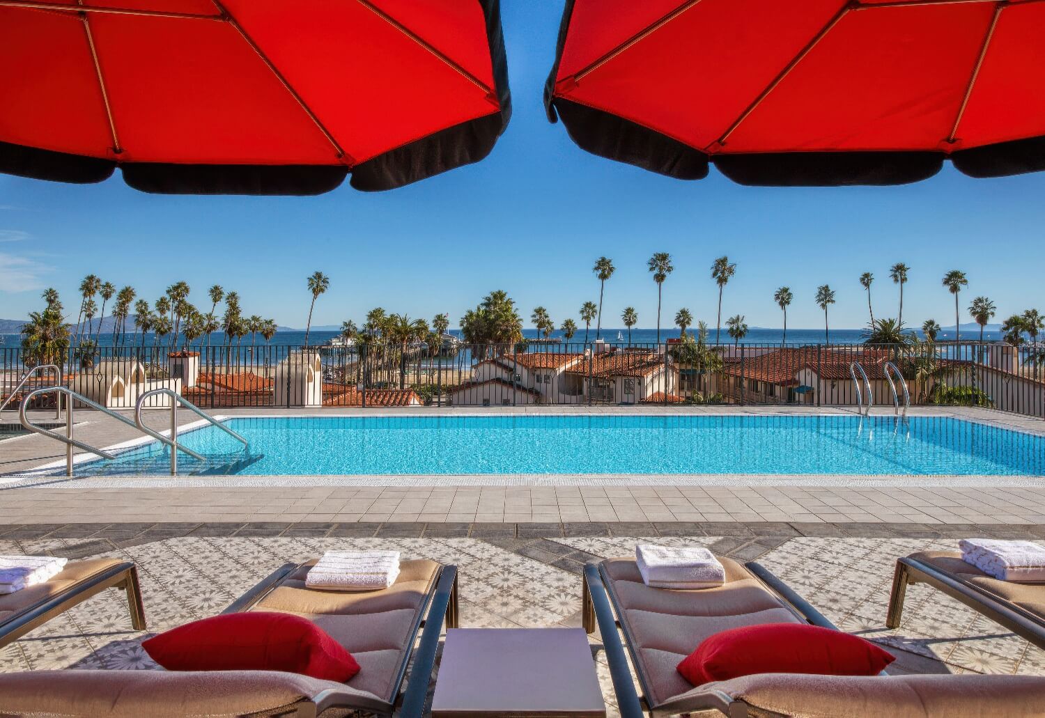 Red umbrellas framing the rooftop pool with palms and the ocean beyond at Hotel Californian, Santa Barbara