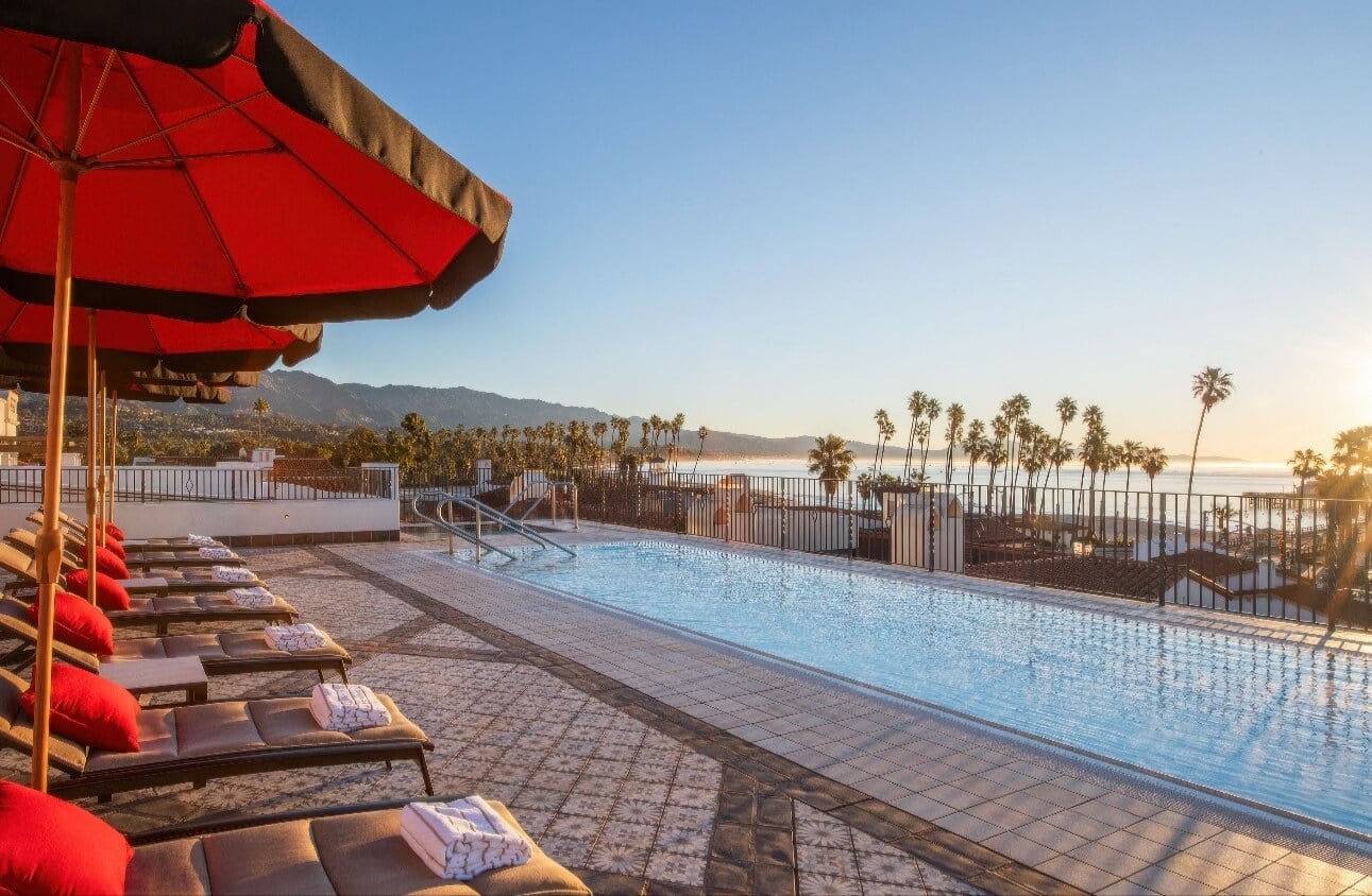 Rooftop pool lined with loungers and red umbrellas facing the mountains at sunset at Hotel Californian, Santa Barbara