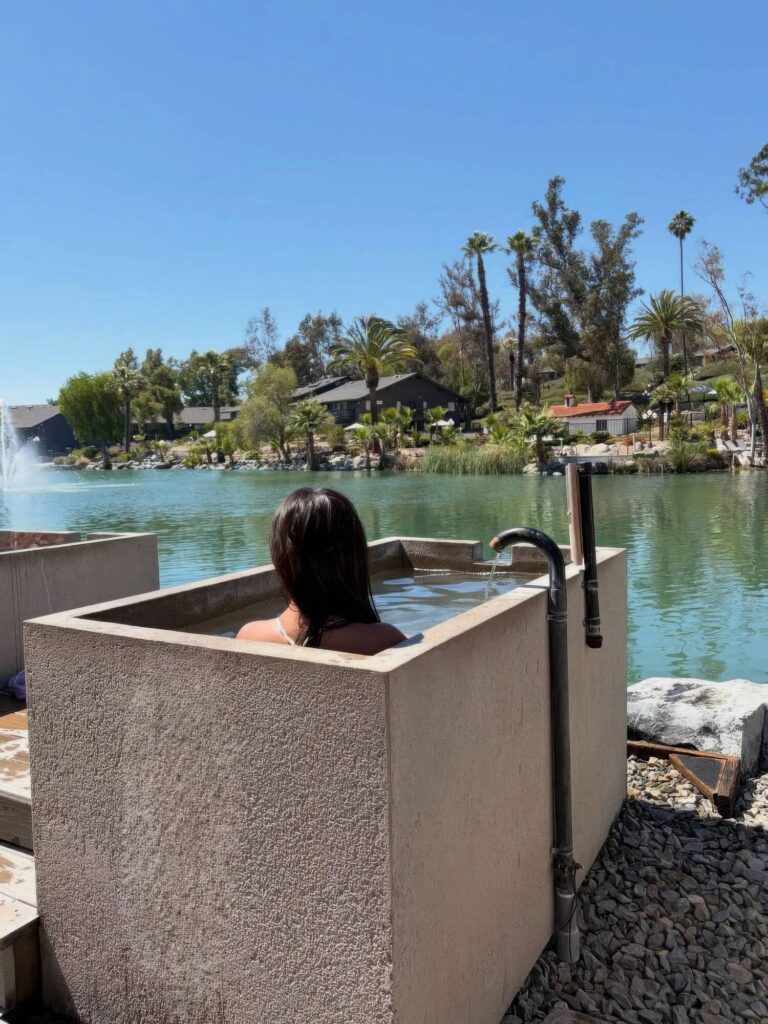 Guest soaking in a private concrete tub fed by a spout beside the lake at Murrieta Hot Springs Resort, California