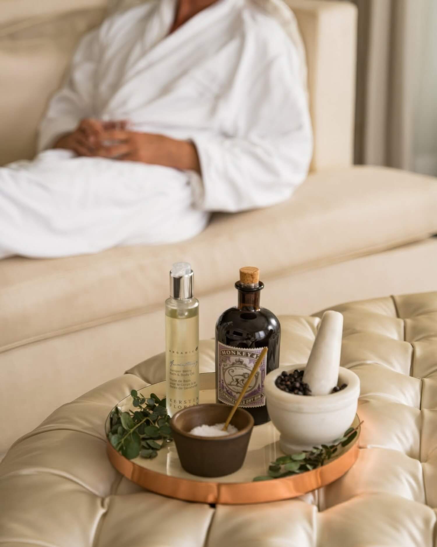 Robed guest behind a Sense Spa ritual tray of bath oil, gin botanicals and juniper berries at Rosewood Miramar Beach, Montecito