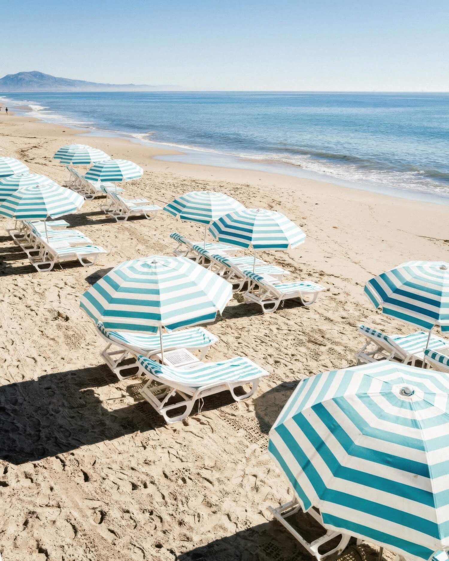 Rows of blue-and-white striped umbrellas and loungers on the sand at Rosewood Miramar Beach, Montecito