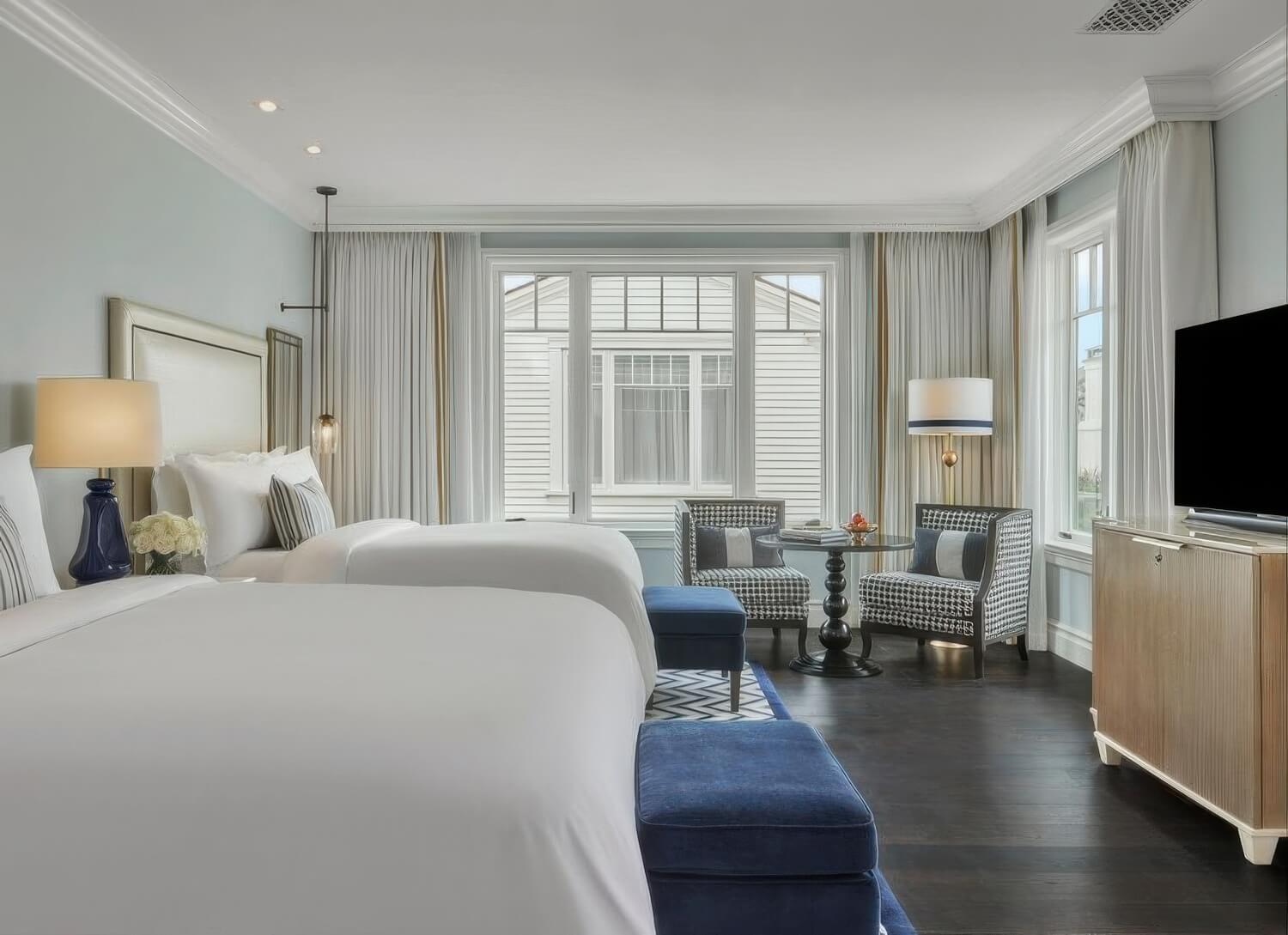 Coastal guest room with two queen beds, navy velvet benches and houndstooth armchairs at Rosewood Miramar Beach, Montecito