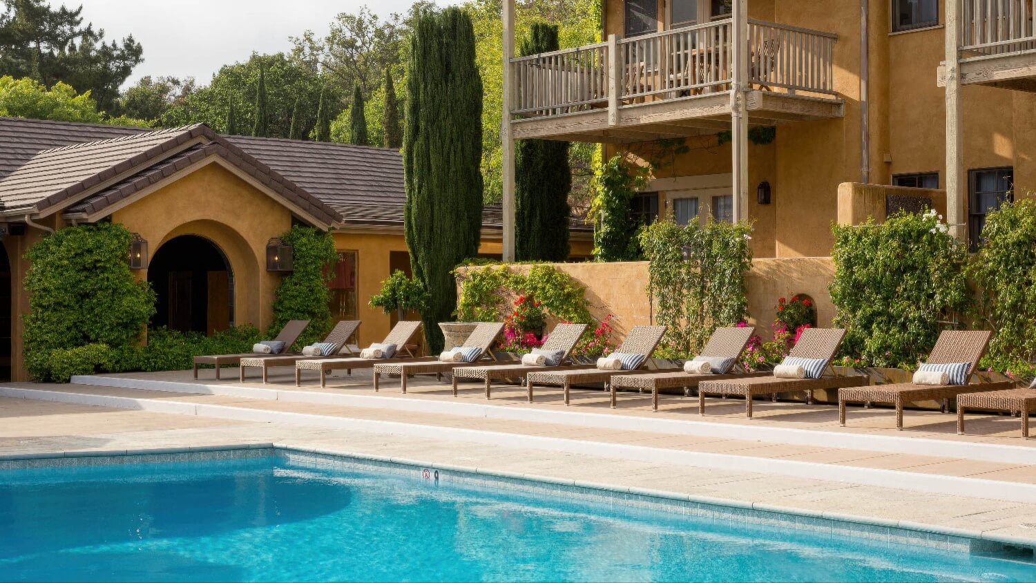 Poolside loungers with rolled towels beneath cypress trees and balconies at Bernardus Lodge and Spa, Carmel Valley