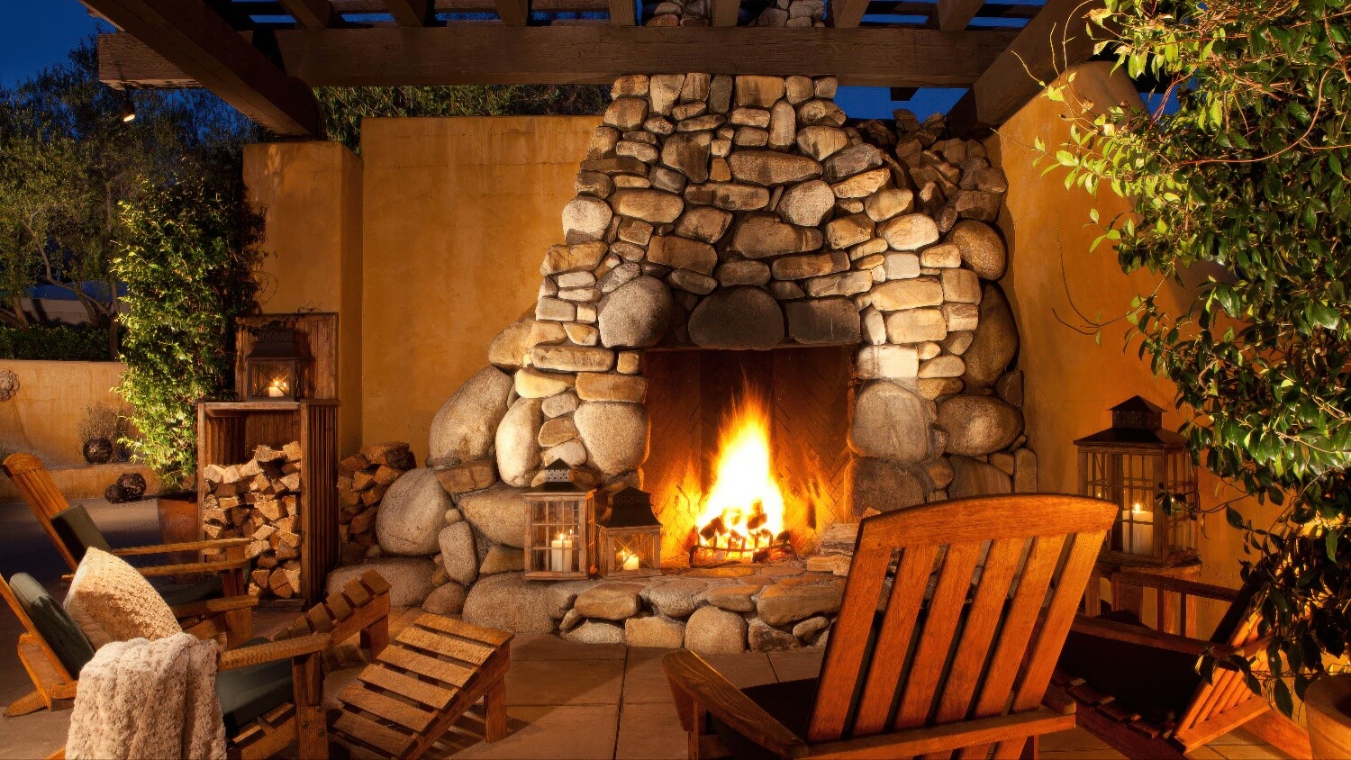 River-stone outdoor fireplace with Adirondack chairs and lanterns at dusk at Bernardus Lodge and Spa, Carmel Valley