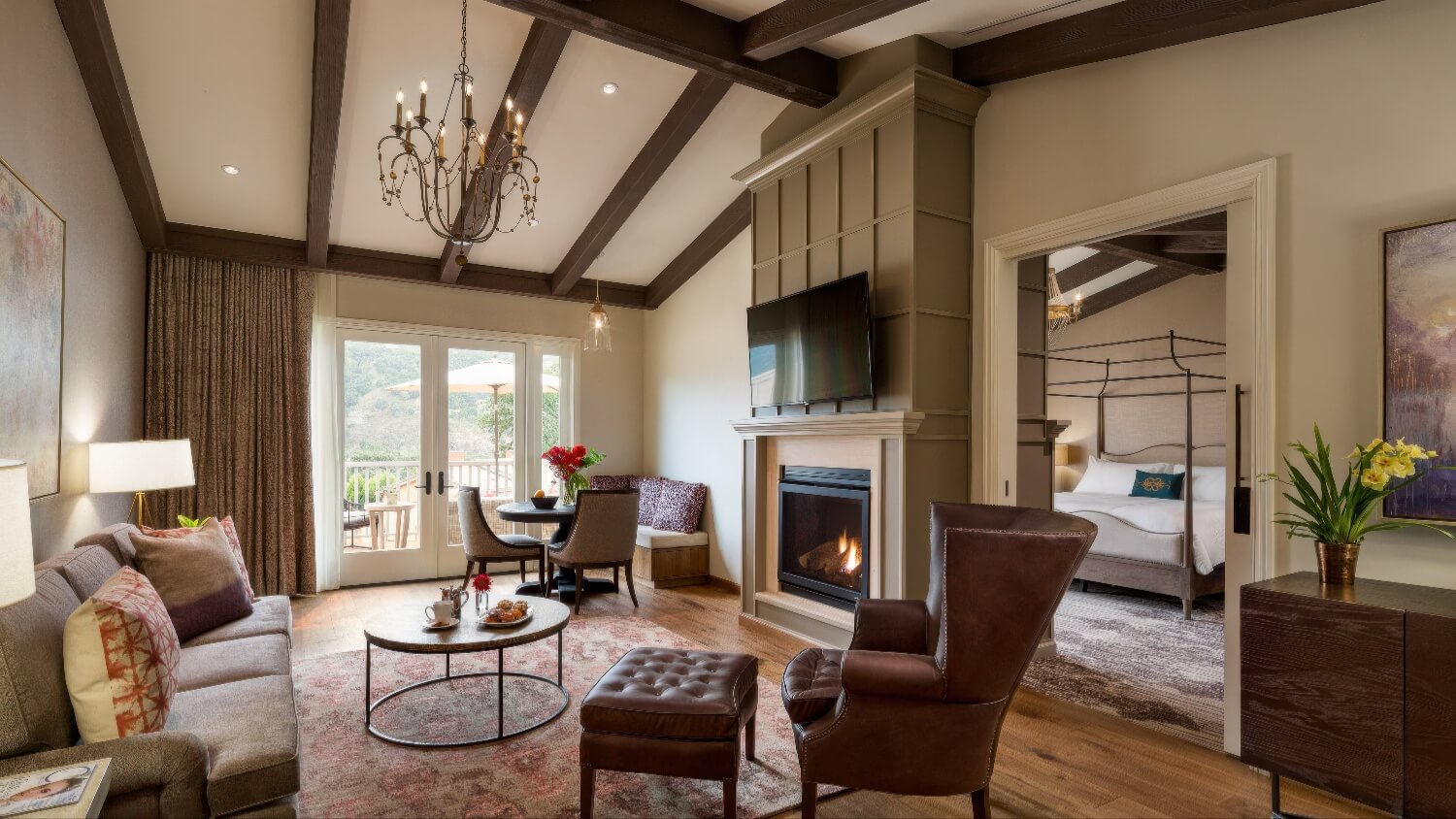 Suite living room with beamed ceiling, fireplace and four-poster bedroom beyond at Bernardus Lodge and Spa, Carmel Valley