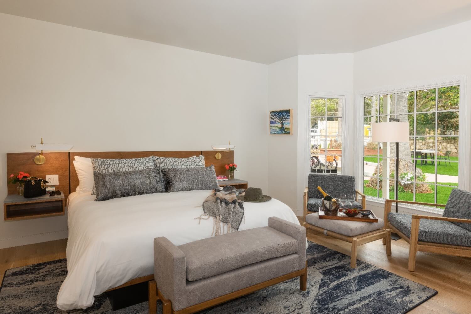 Guest room with sitting area, champagne tray and bay window onto the lawn at Carmel Beach Hotel, Carmel-by-the-Sea