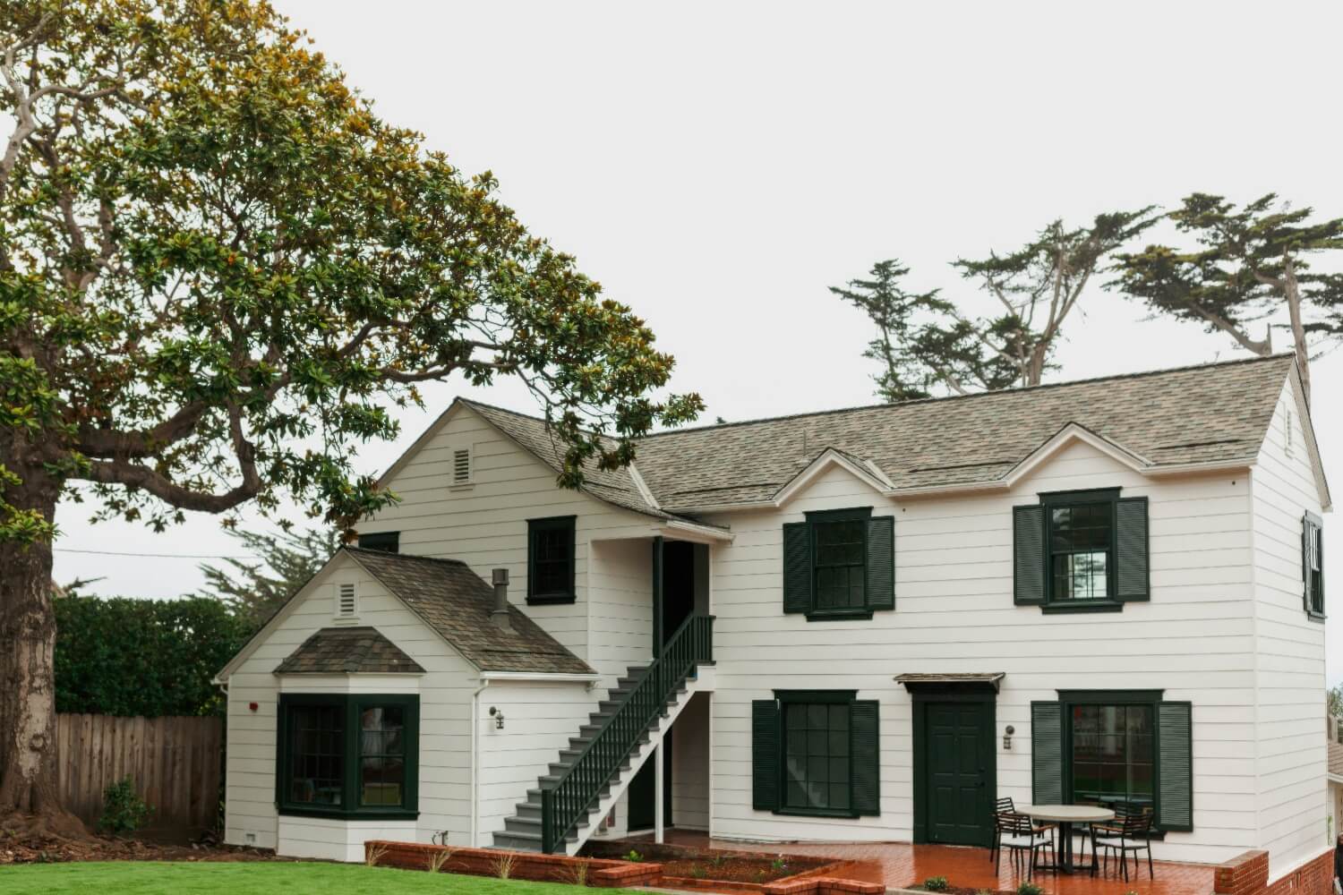 White clapboard guest building with green shutters, exterior stair and magnolia tree at Carmel Beach Hotel, Carmel-by-the-Sea